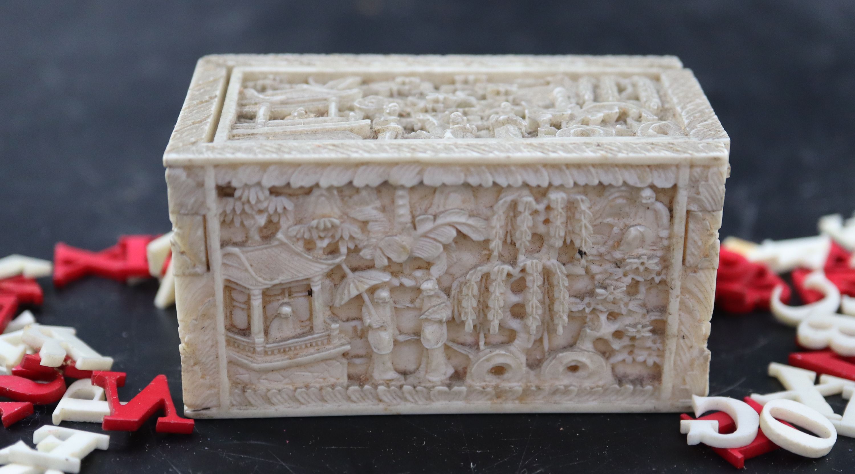 A 19th century Chinese relief carved ivory box housing plain and red stained ivory alphabet letters, 6.75cm